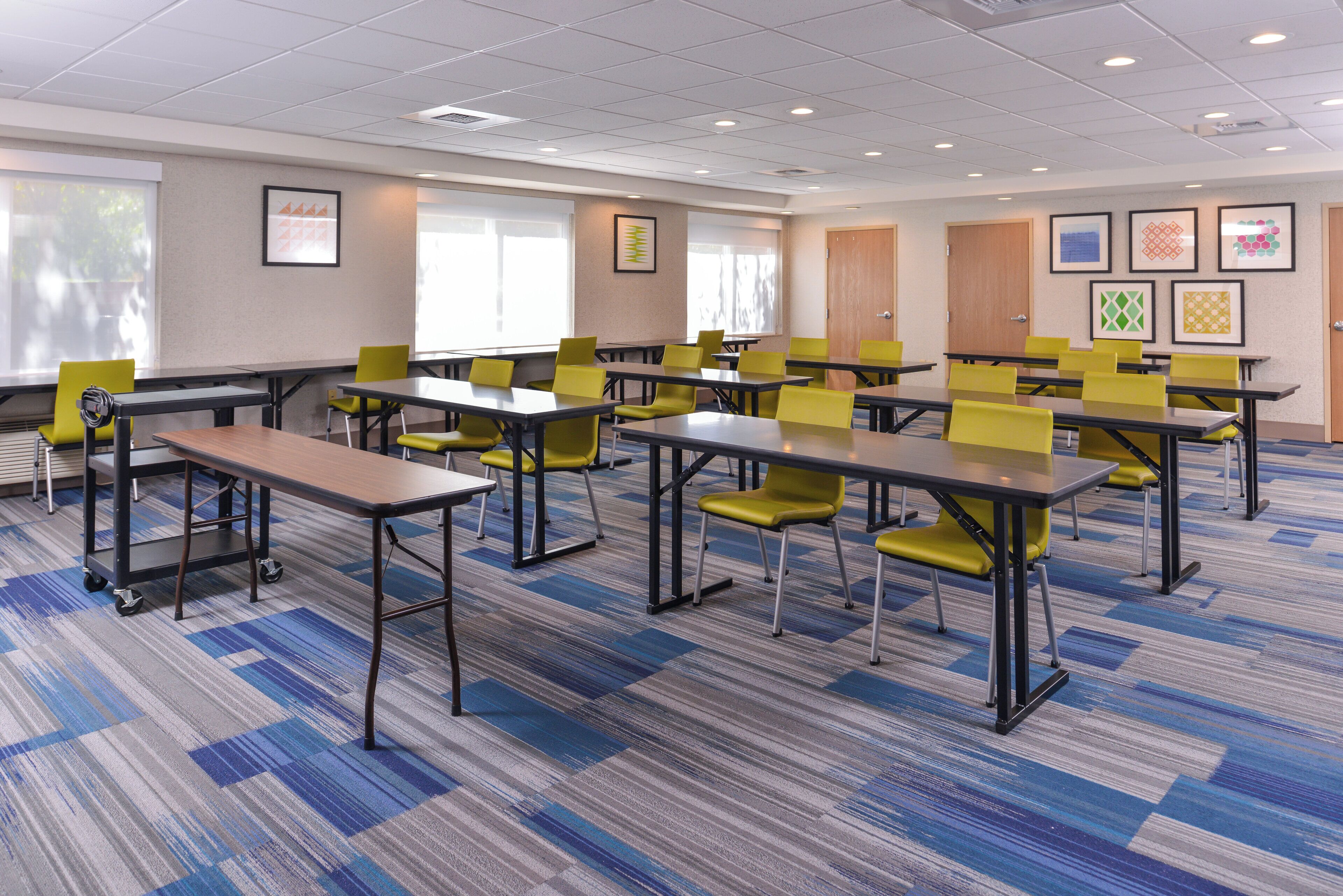 A conference room with multiple tables and chairs, carpeted flooring, and framed artwork on the walls.