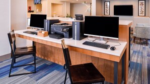 A hotel reception desk with two monitors, a printer, a keyboard, and a computer. There are two chairs, a carpeted floor, and a framed picture on the wall. - Holiday Inn Express & Suites Lacey – Olympia by IHG (Lacey)