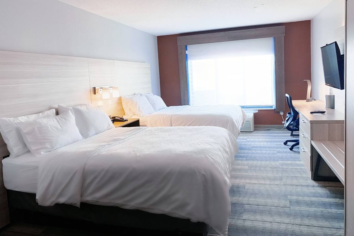 A hotel room with two beds, a desk with a chair, a television, and a window.