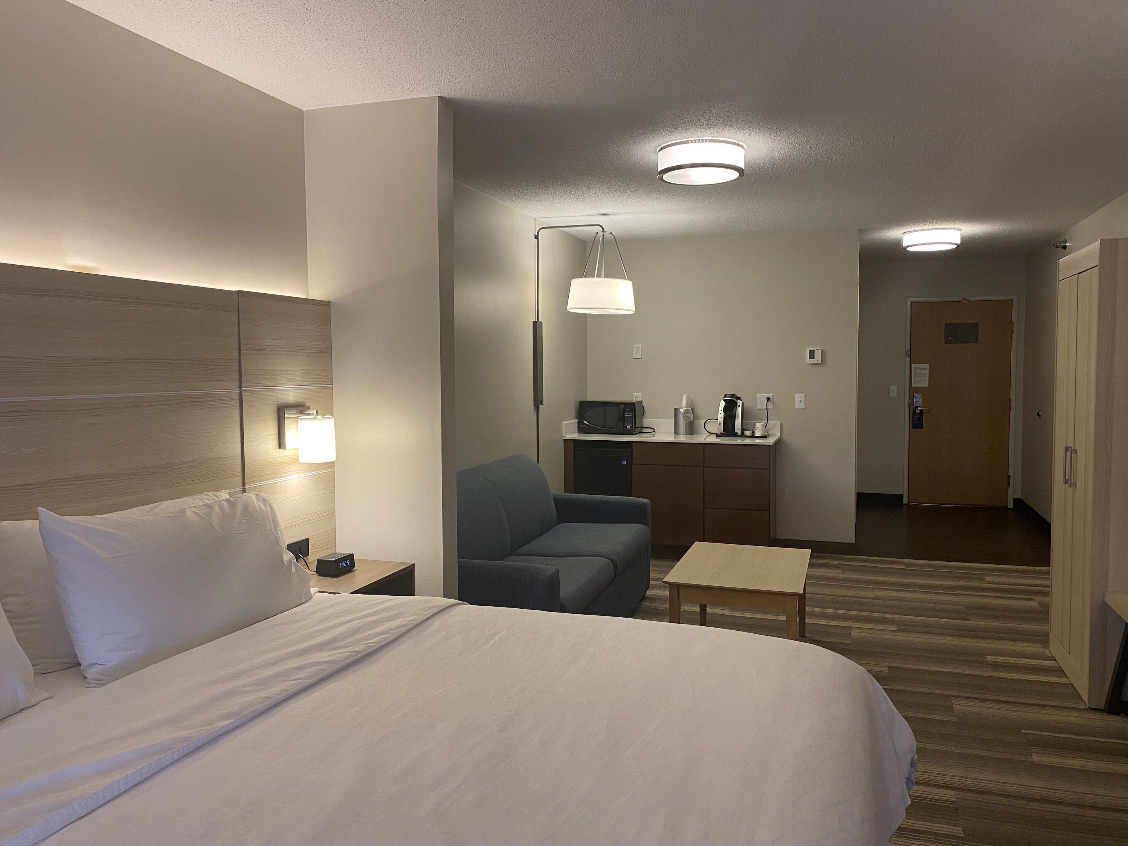 Une chambre d’hôtel équipée d’un lit, d’un bureau, d’une chaise, d’un four à micro-ondes, d’une machine à café et d’une porte.