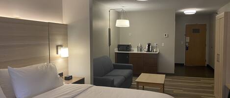 Une chambre d’hôtel équipée d’un lit, d’un bureau, d’une chaise, d’un four à micro-ondes, d’une machine à café et d’une porte.