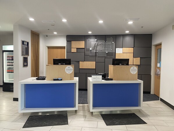 A hotel reception area with two reception desks, a vending machine, and a wall-mounted sign indicating the Holiday Inn Express & Suites. - Holiday Inn Express Hotel & Suites Logansport by IHG (Logansport)