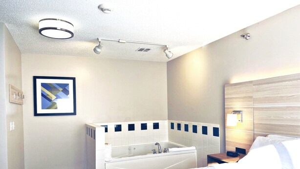 Une chambre d’hôtel avec un grand lit, une douche séparée, un tableau encadré au mur et une table de chevet avec une lampe.
