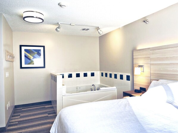 Ein Hotelzimmer mit einem großen Bett, einer separaten Dusche, einem gerahmten Bild an der Wand und einem Nachttisch mit Lampe.