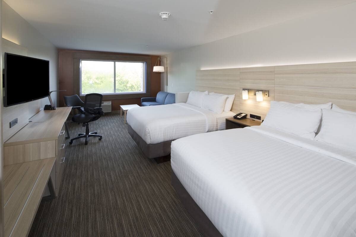 A hotel room with two beds, a desk with a computer, a TV, and a window with a view of greenery.