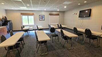 A conference room with multiple tables and chairs, a projector screen, and a television on the wall.