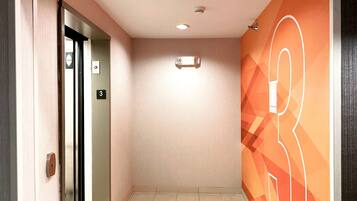 Un couloir avec une porte portant le numéro « 3 », un luminaire au plafond et un motif géométrique sur le mur.