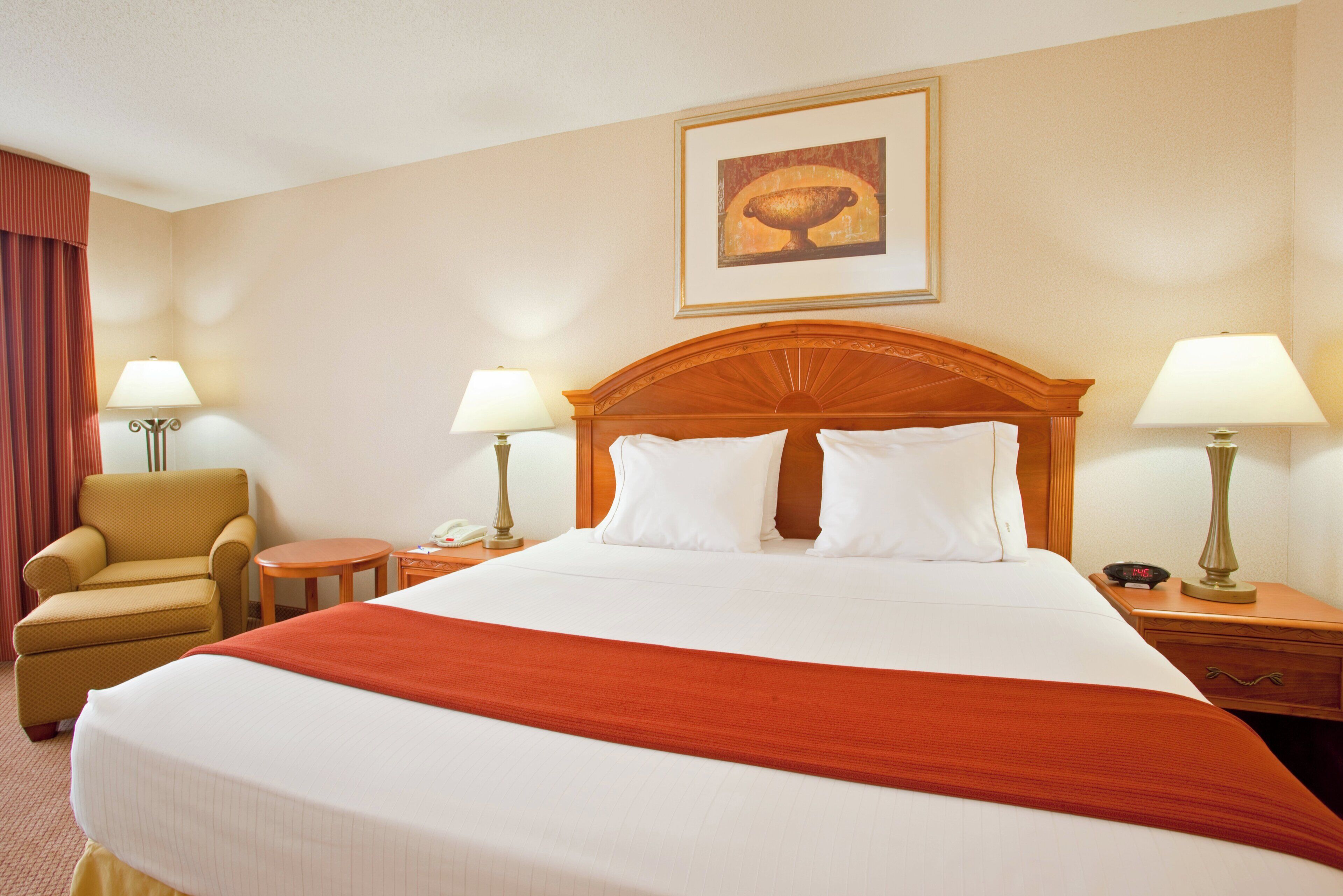 A hotel room with a large bed, two bedside tables with lamps, a chair, and a painting on the wall.