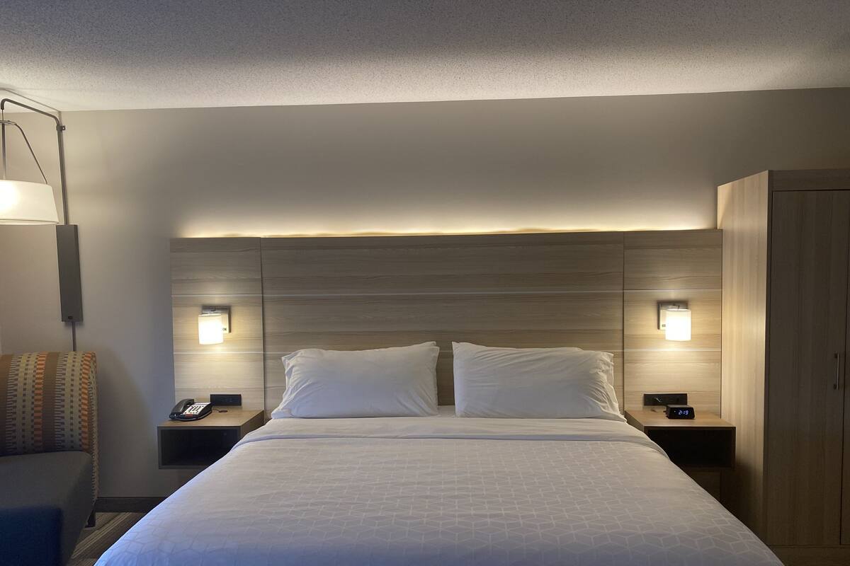 A hotel room with a large bed, two bedside tables with lamps, a nightstand, a chair, and a wardrobe.