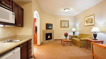 A living room with a fireplace, a television, a sofa, a coffee table, and a kitchen area with a microwave.