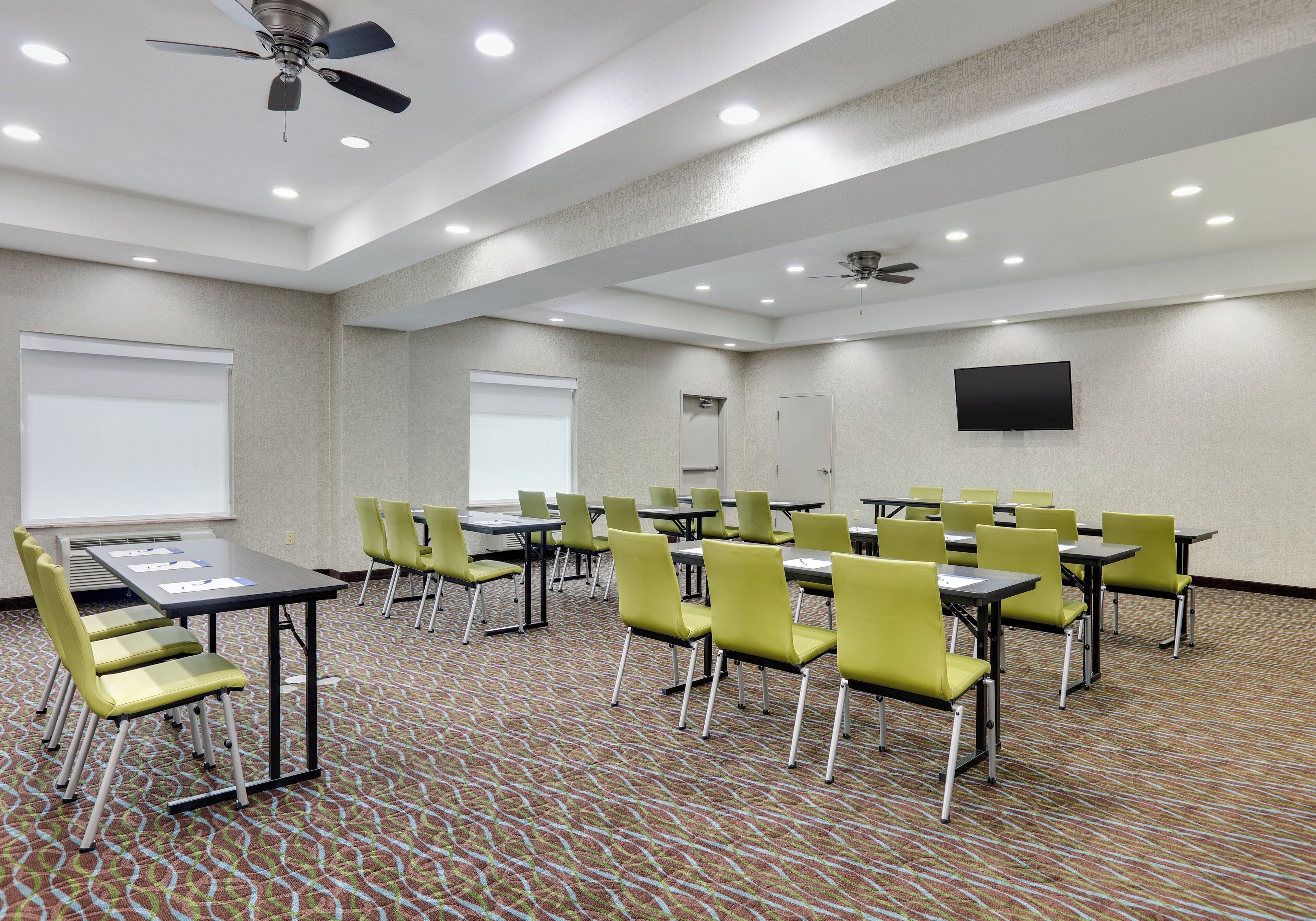 A conference room with tables and chairs, ceiling fans, recessed lighting, and a flat-screen TV on the wall.