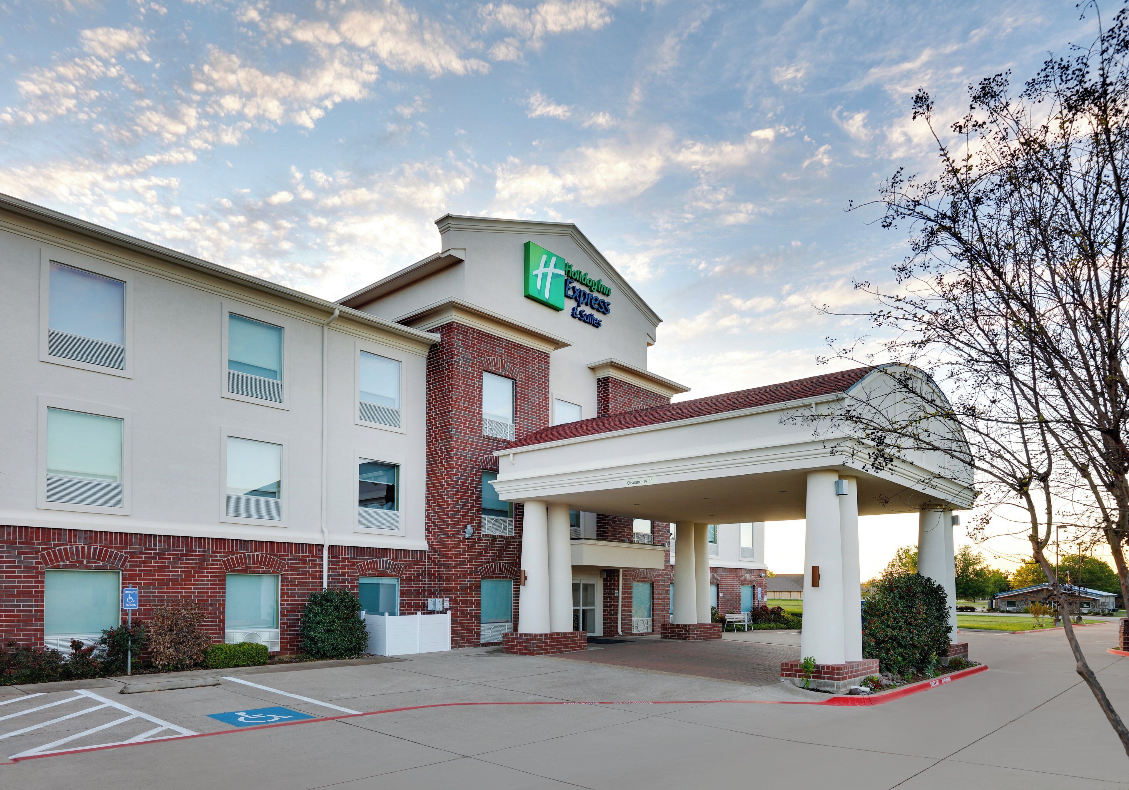 Um hotel Holiday Inn Express com entrada coberta, placa indicando vaga para deficientes e céu claro.