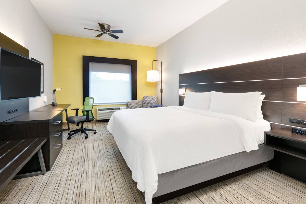 A hotel room with a bed, desk, chair, TV, and a ceiling fan.