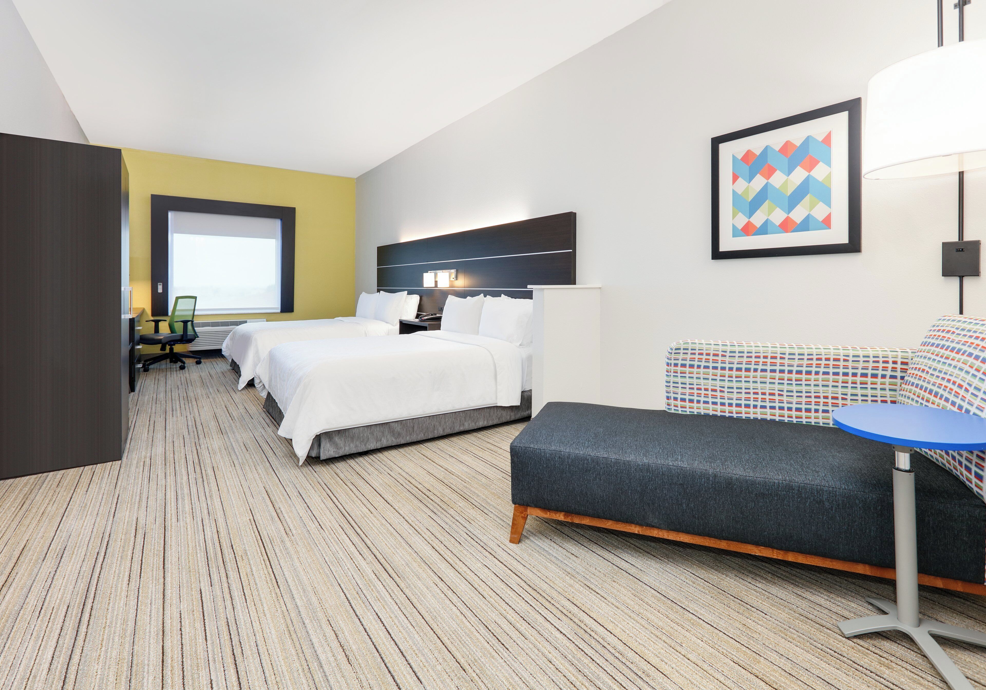 A hotel room with two beds, a sofa, a small table, and a window.