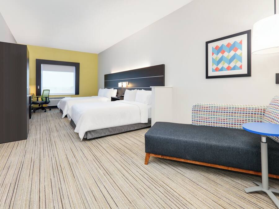 A hotel room with two beds, a sofa, a small table, and a window.