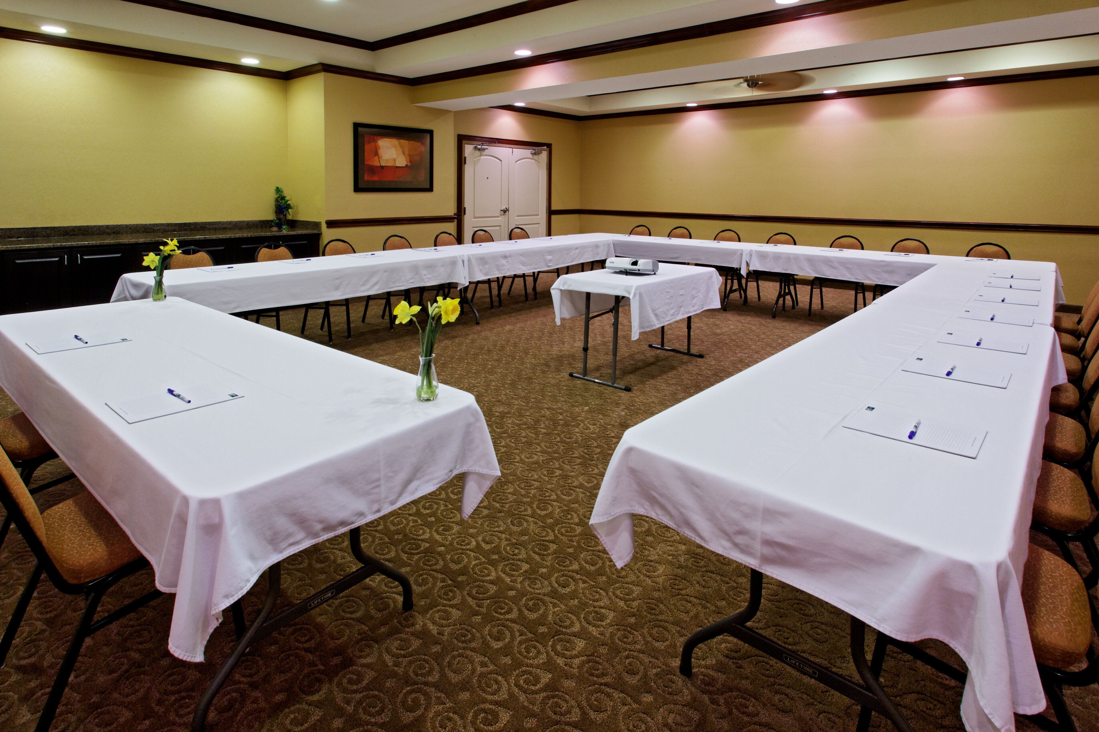 A conference room with long tables, chairs, and a carpeted floor.
