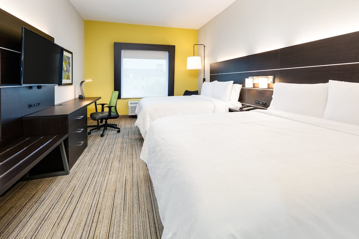 A hotel room with two beds, a desk, a chair, a TV, and a window.