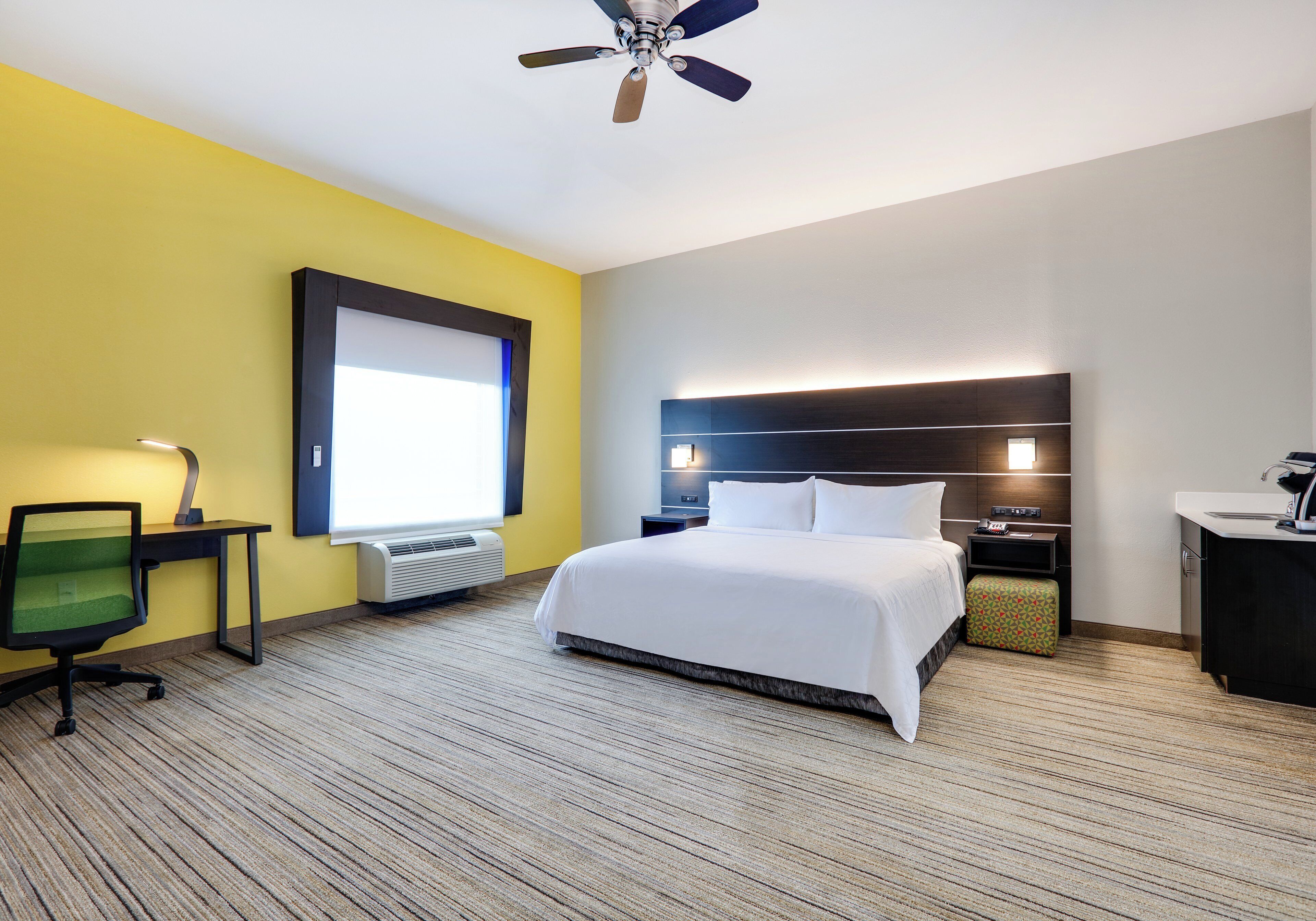 A hotel room with a bed, desk, chair, and a ceiling fan.