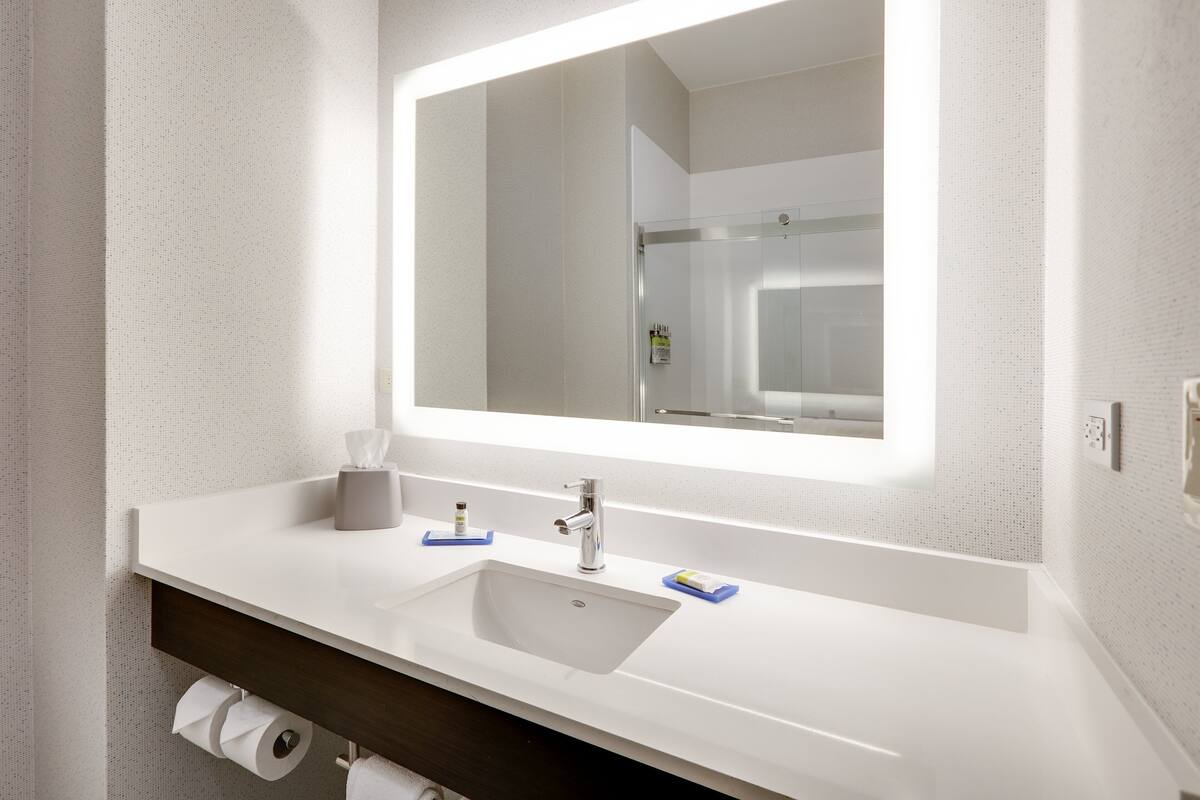 A modern bathroom with a large mirror, white sink, and dark wooden vanity.