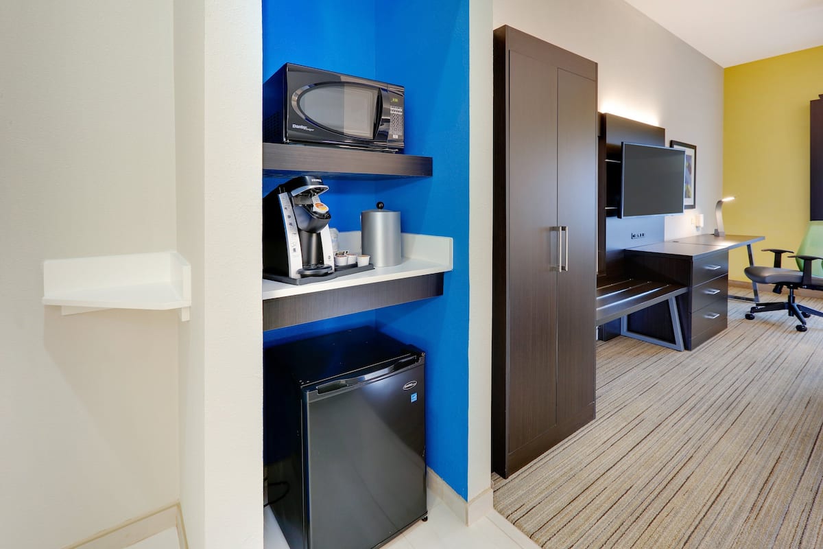 A compact hotel room with a kitchenette, a flat-screen TV, a desk, and a chair.