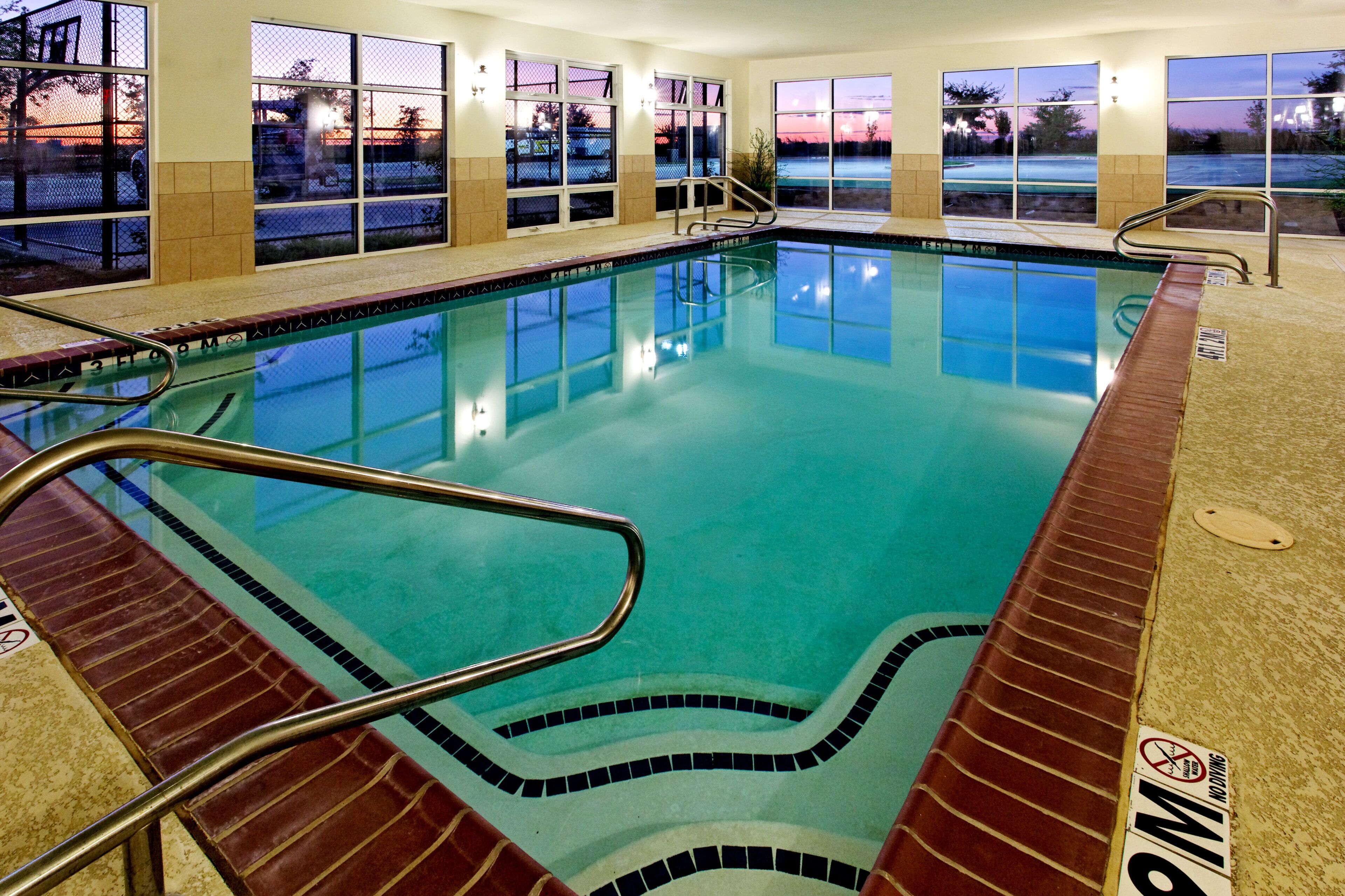 An indoor swimming pool with clear water, surrounded by windows.