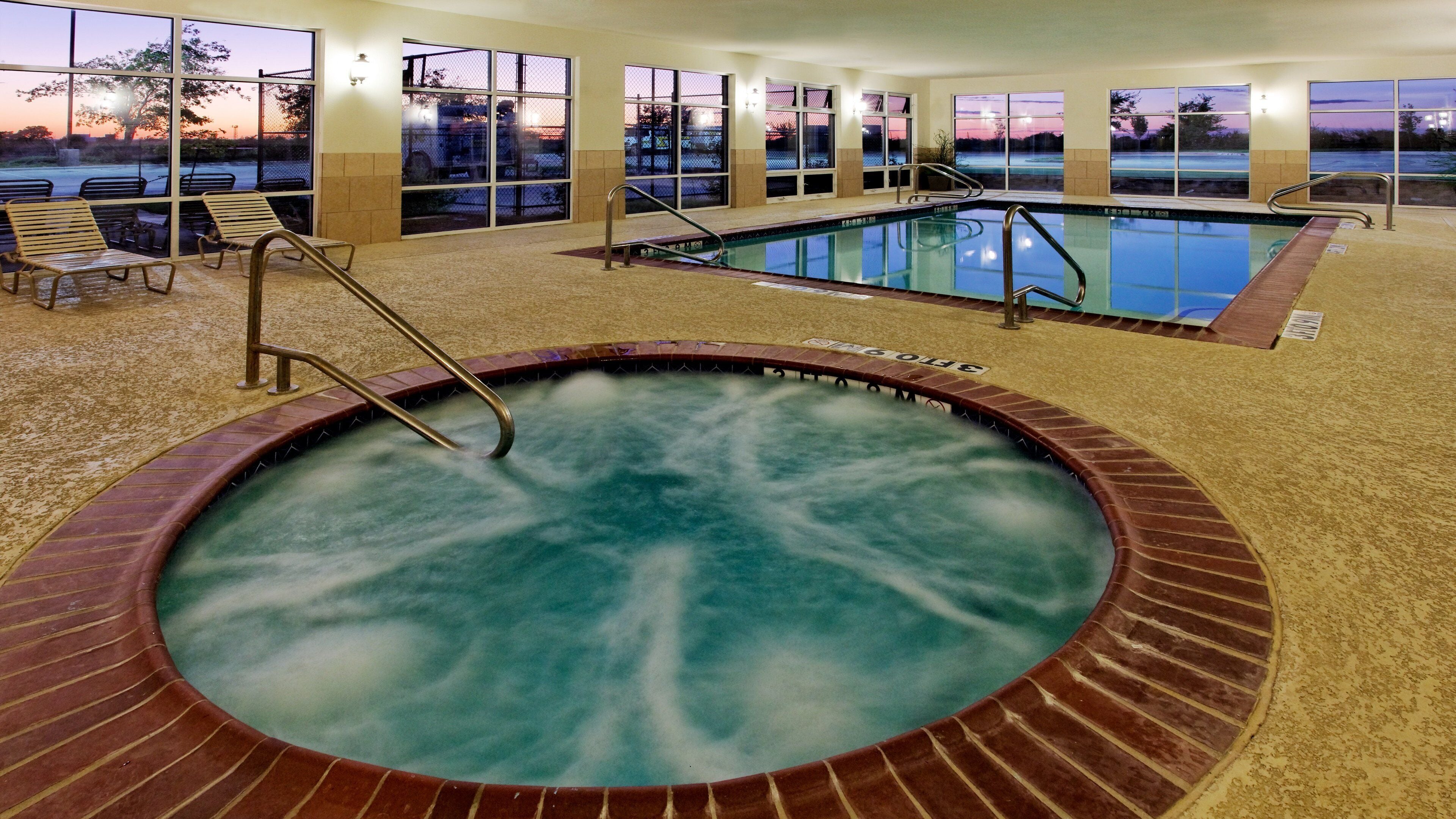 Una piscina interior con un jacuzzi, rodeada de ventanas con vistas a la puesta de sol.