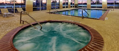 Una piscina interior con un jacuzzi, rodeada de ventanas con vistas a la puesta de sol.