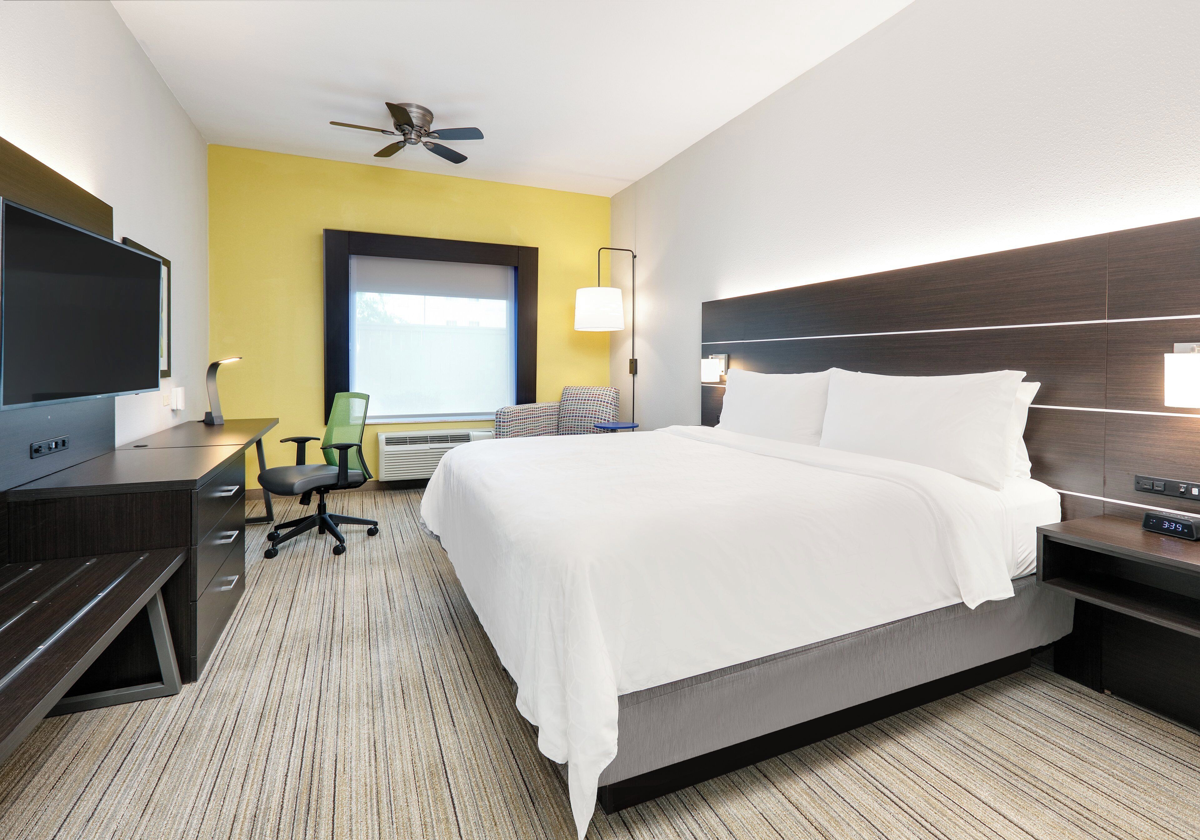 Une chambre d’hôtel équipée d’un lit, d’un bureau, d’une chaise, d’une télévision et d’un ventilateur de plafond.