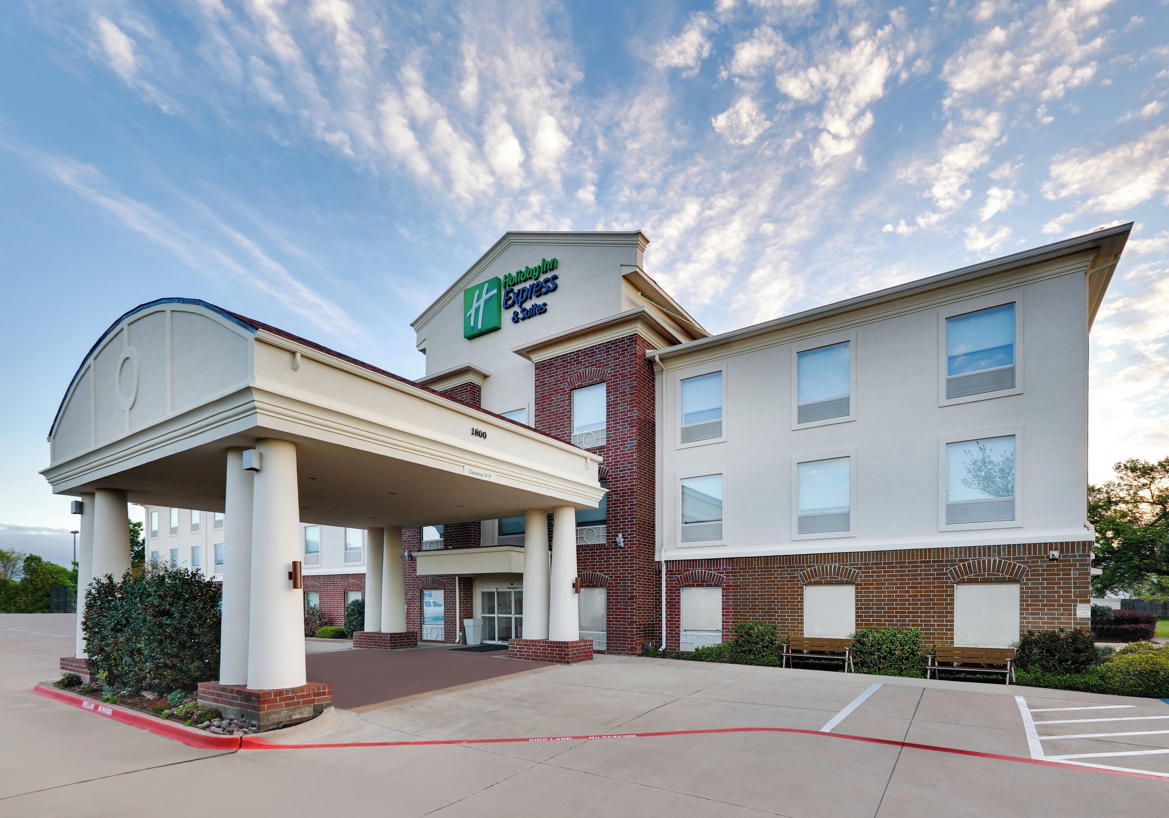 Um Holiday Inn Express & Suites com entrada coberta, fachada de tijolos e céu claro.