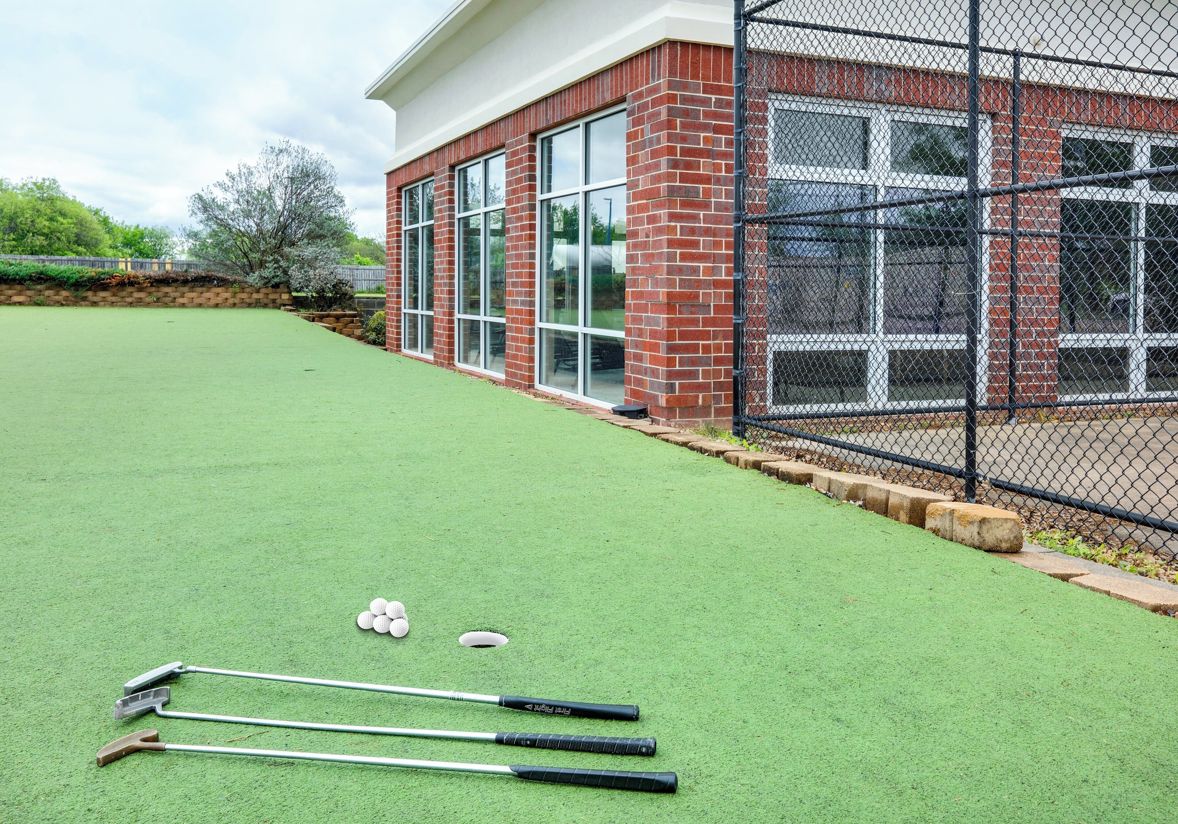 A green artificial turf area with croquet equipment and a brick building with large windows.