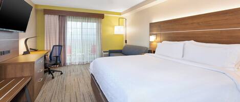 A hotel room with a bed, a desk, a chair, a television, and a ceiling fan.
