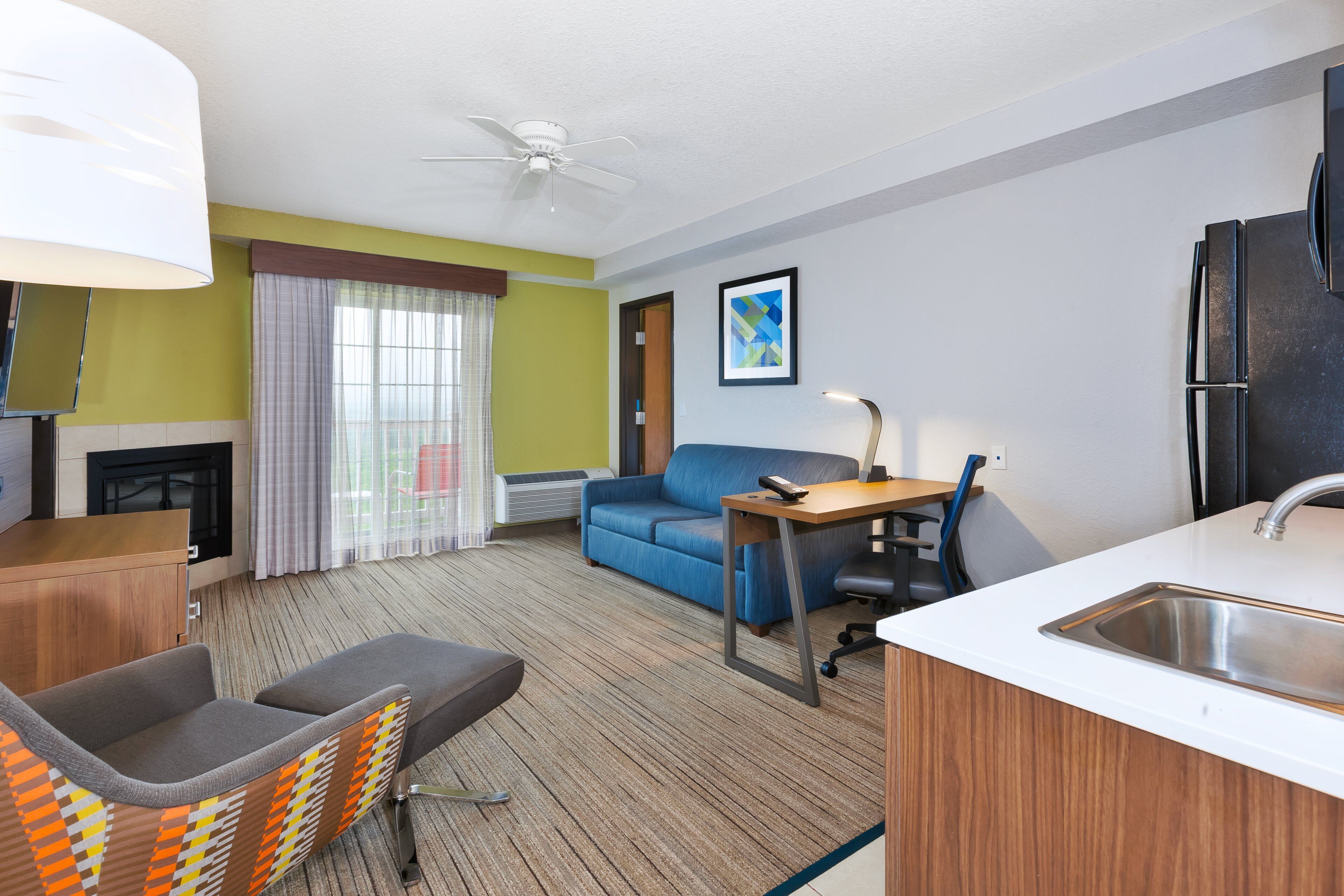 A hotel room with a kitchenette, a sofa, a desk, and a chair.