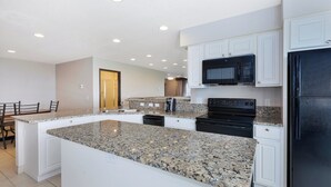 A modern kitchen with granite countertops, white cabinetry, a black refrigerator, and a built-in microwave. - Holiday Inn Express & Suites Petoskey by IHG (Petoskey)