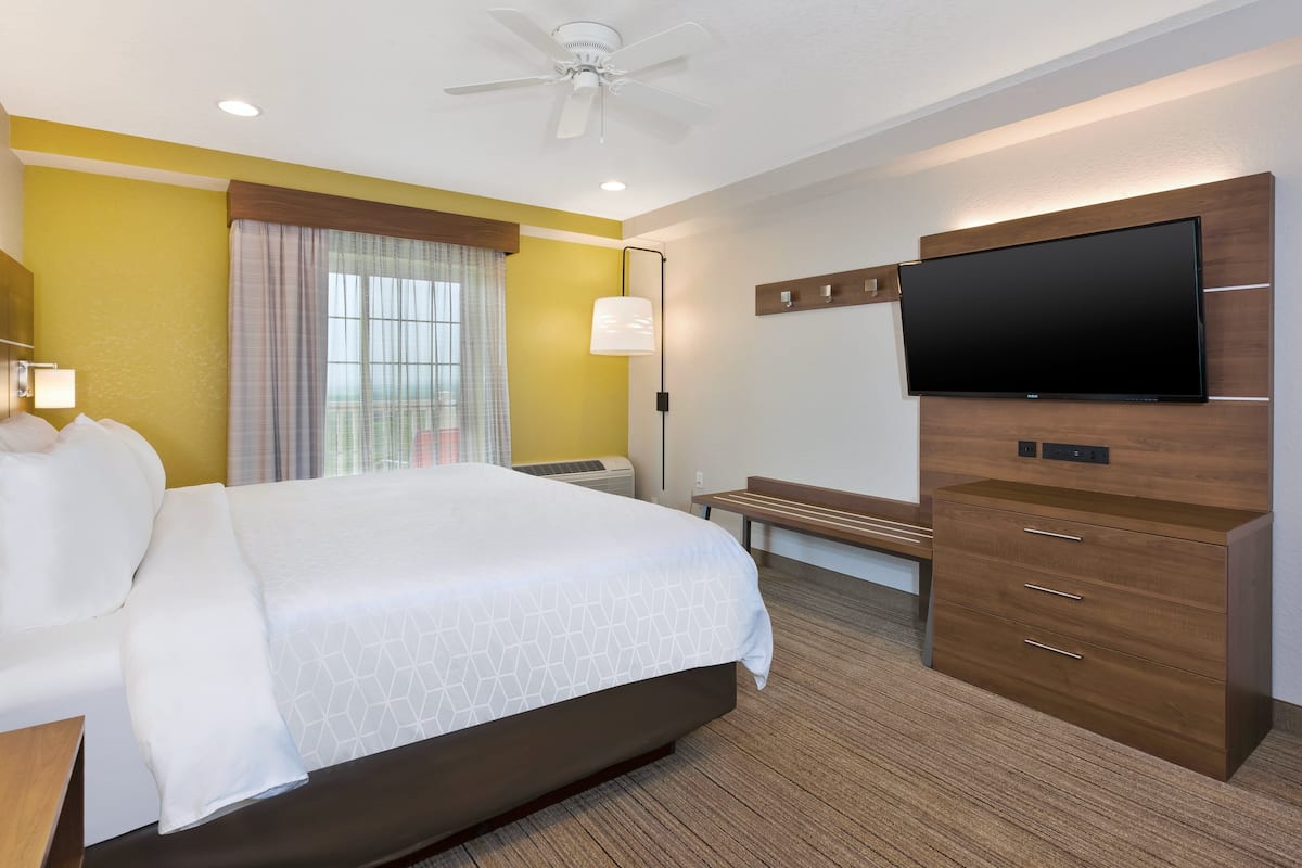 Habitación de hotel con una cama grande, un televisor de pantalla plana montado en la pared, un escritorio con lámpara y un ventilador de techo.