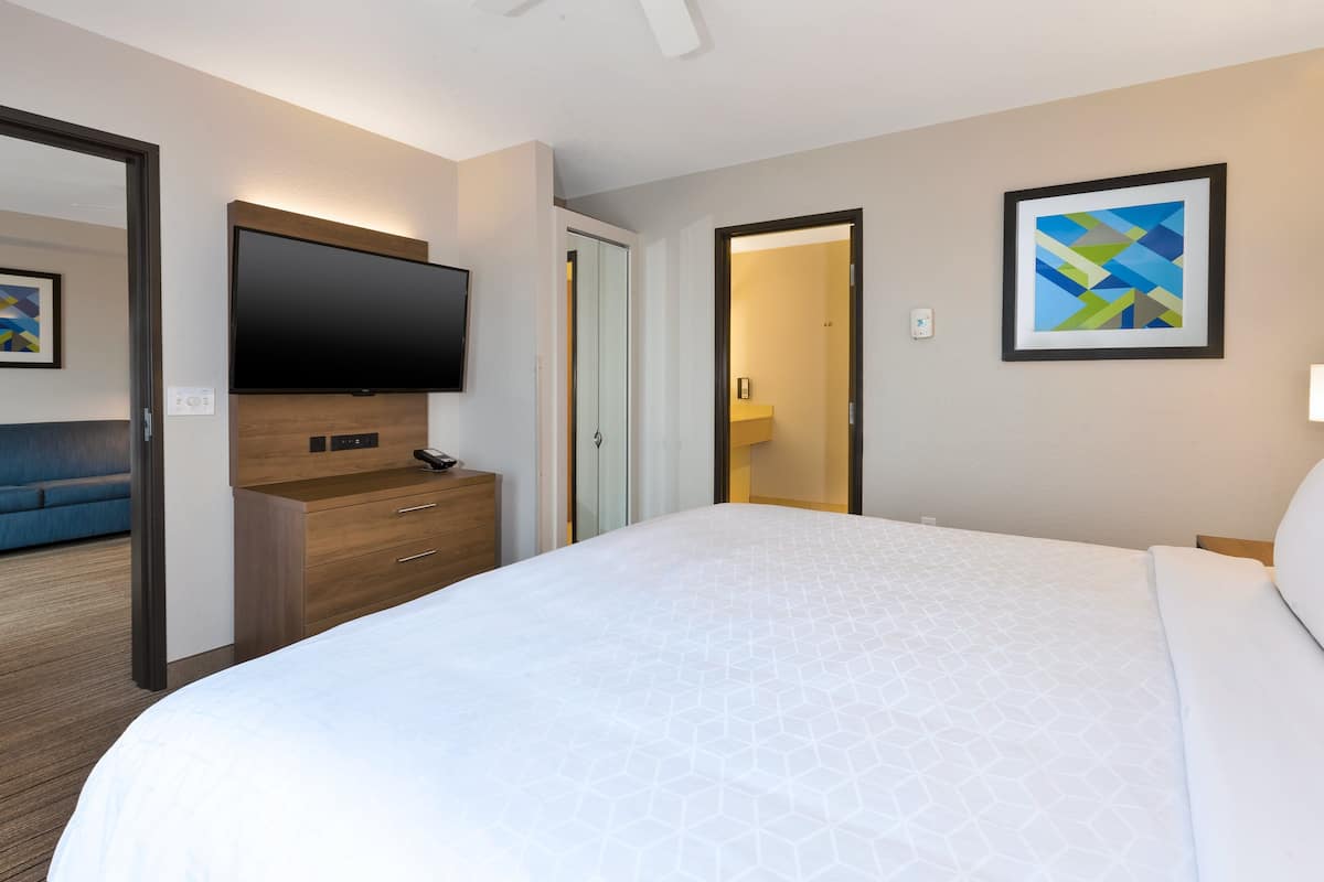 Un cuarto de hotel con una cama grande, un televisor de pantalla plana montado en la pared, un aparador de madera y una obra de arte abstracta enmarcada.