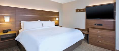 A hotel room with a large bed, a flat-screen TV, wooden headboard, bedside tables, and a carpeted floor.