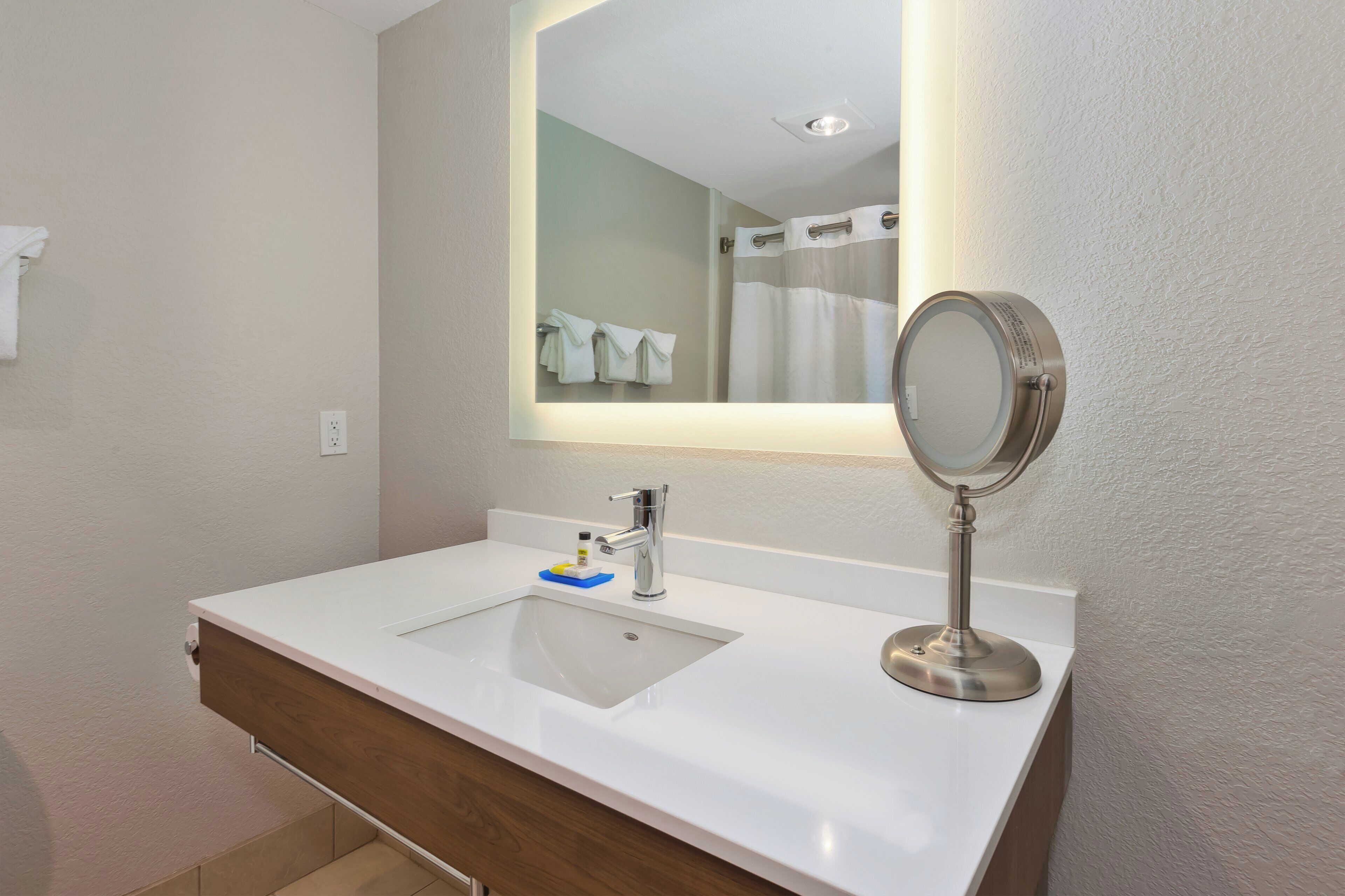 A modern bathroom with a white sink, a mirror, and a shower curtain.