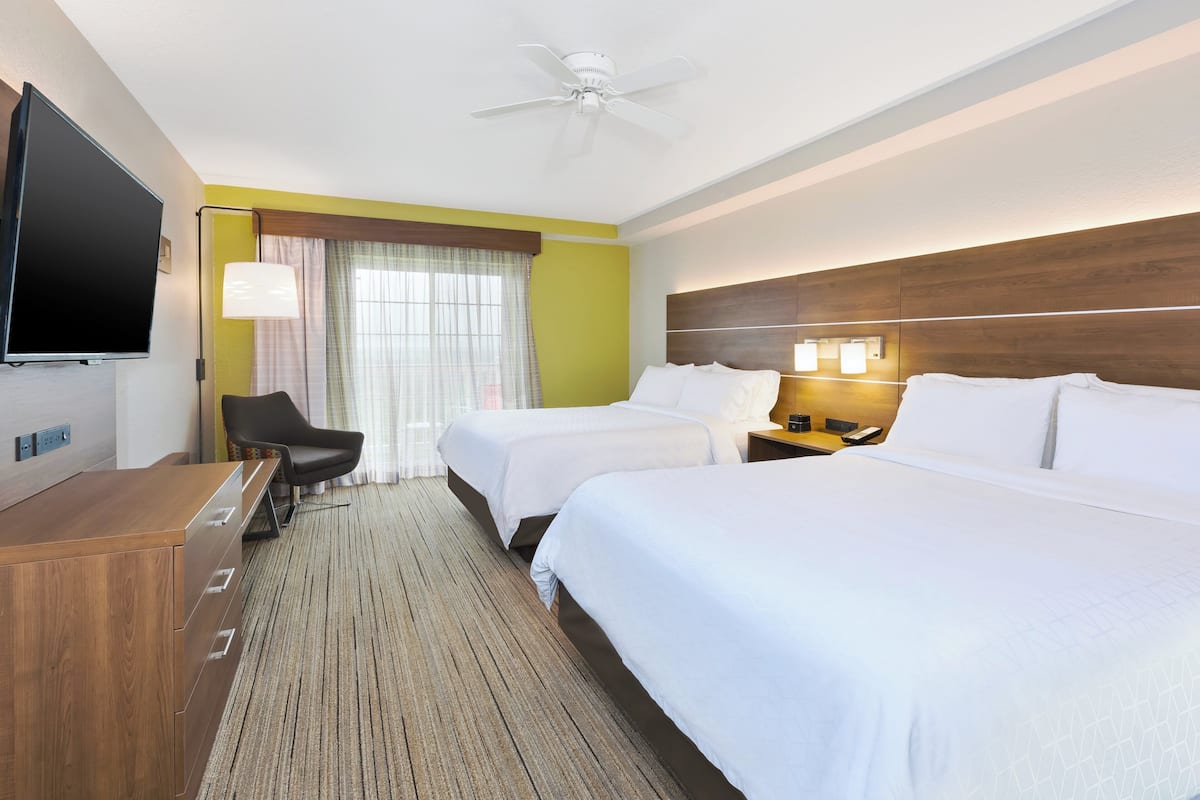 Habitación de hotel con dos camas, un escritorio, una silla, un televisor y un ventilador de techo.