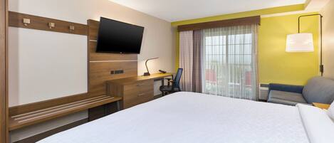 Habitación de hotel con cama, escritorio, silla, televisor y ventana con cortinas.