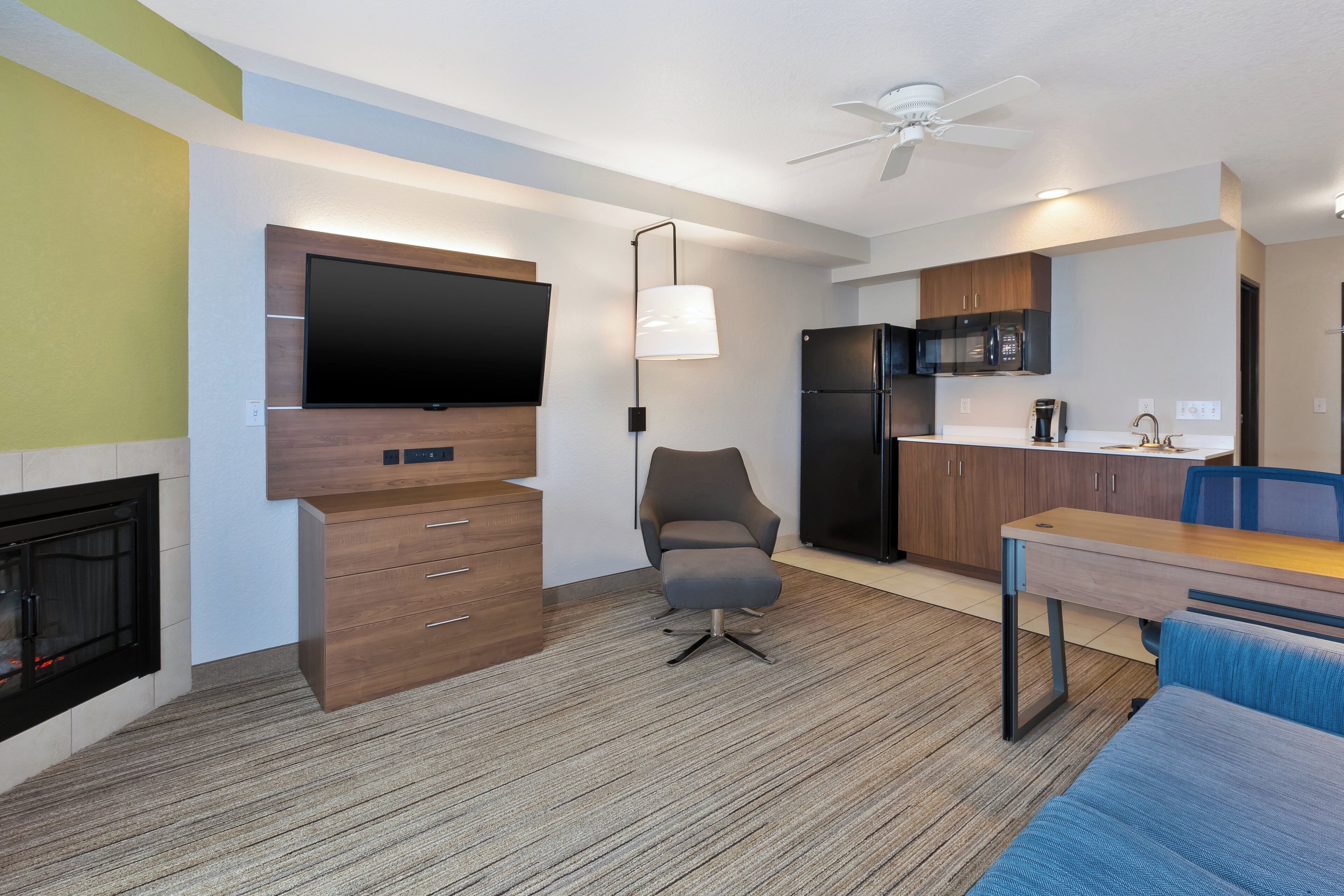 A modern kitchen with a flat-screen TV, wooden cabinetry, a refrigerator, and a dining area with a table and chairs.