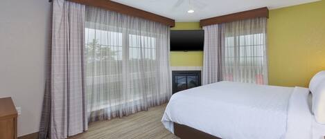 Habitación de hotel con cama, cortinas, ventilador de techo, televisor de pantalla plana y chimenea.