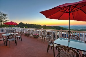 Une terrasse extérieure avec des tables et des chaises, des parasols rouges et une vue sur le paysage.