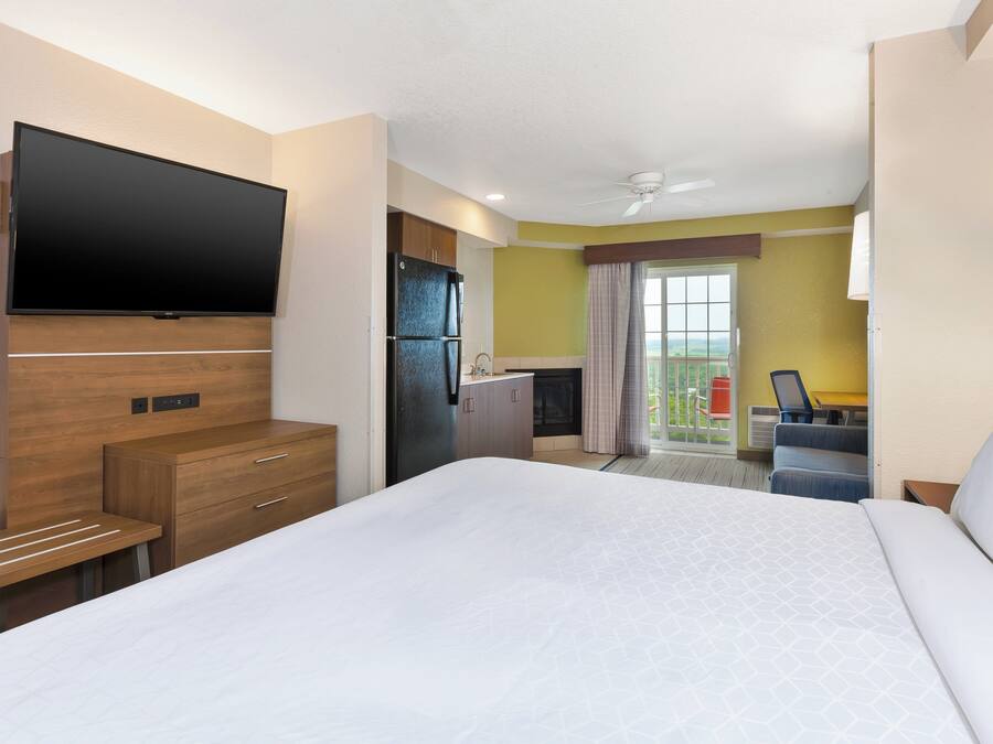 A hotel room with a bed, a flat-screen TV, a kitchenette, and a balcony with a view.