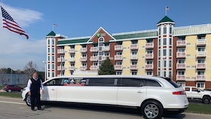 Une limousine blanche était garée devant un grand hôtel à plusieurs étages, doté de balcons et d’un toit végétalisé.