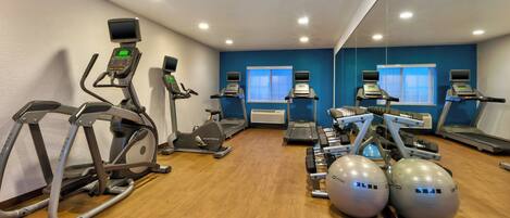Un gimnasio con diversos equipos de ejercicio, incluyendo cintas de correr, elípticas y pesas libres.