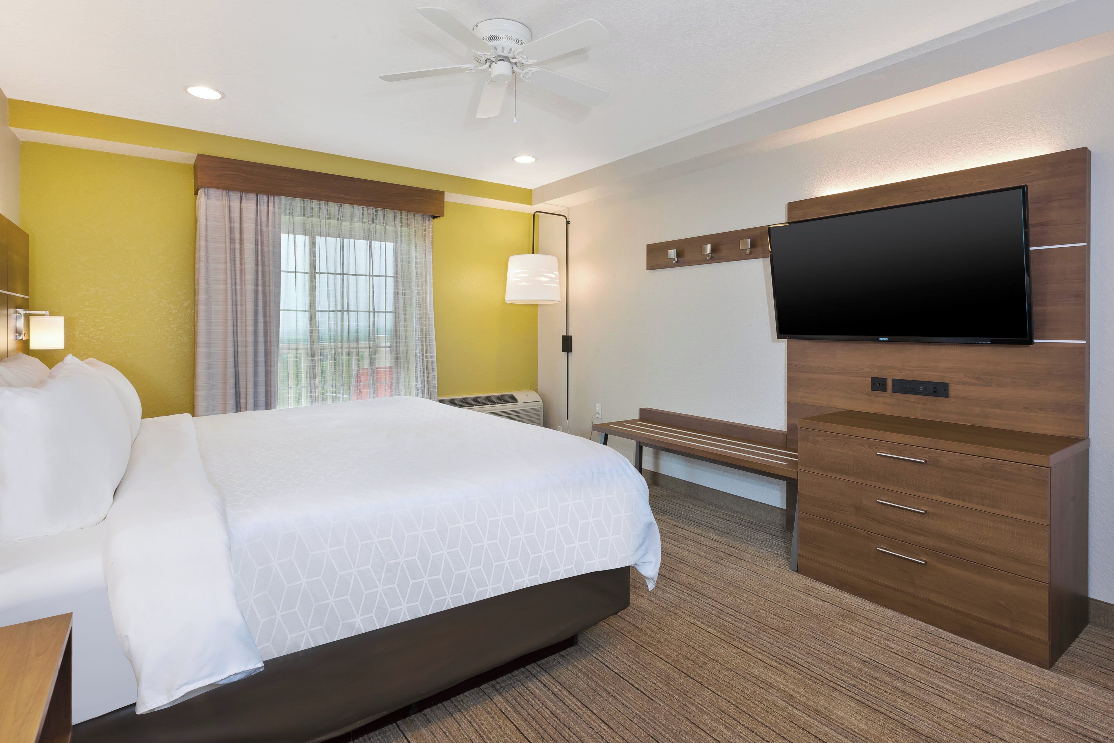 A hotel room with a bed, a desk, a television, and a ceiling fan.