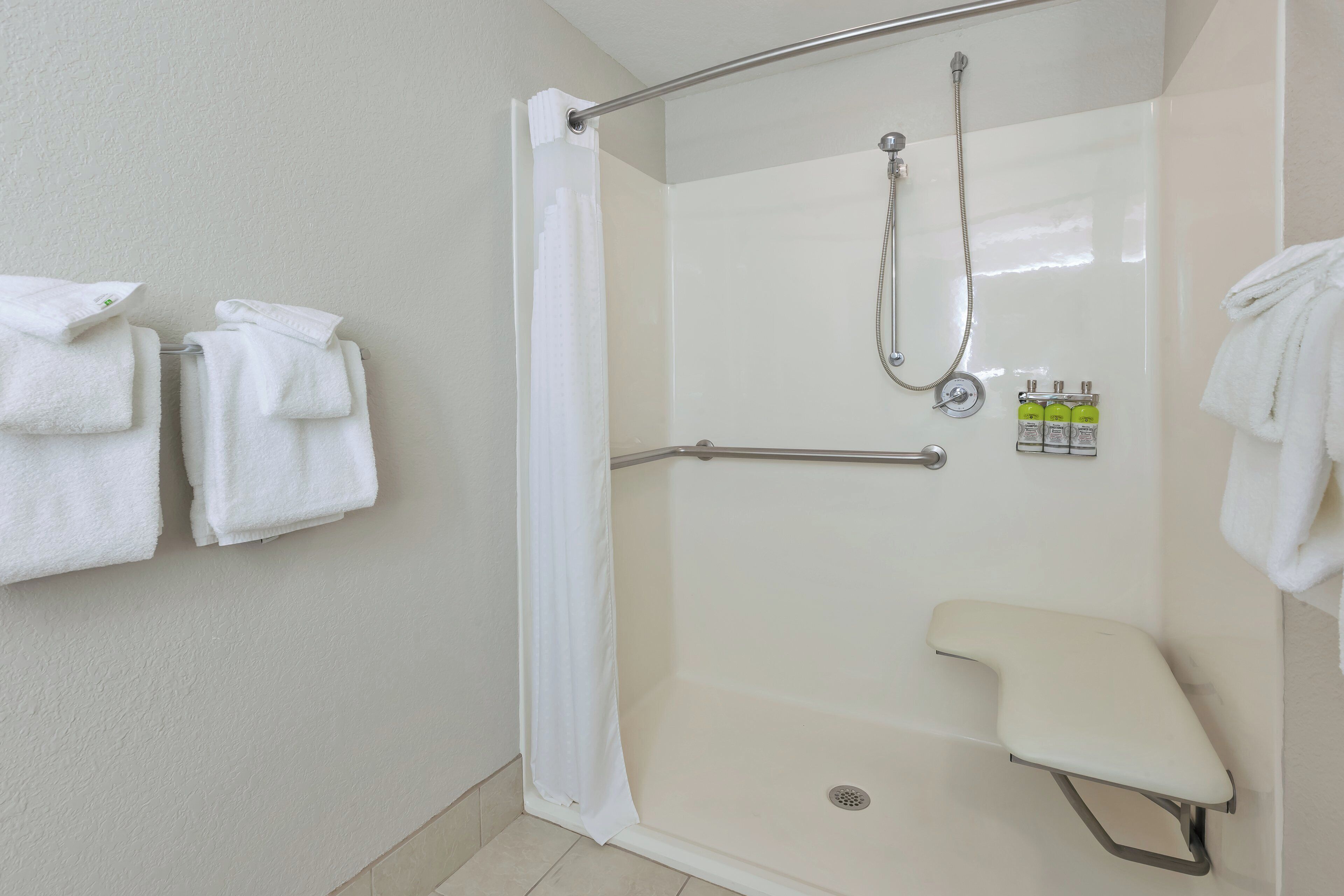 Un espace douche doté d’une porte en verre, d’un pommeau de douche, d’un flexible de douche et d’un porte-serviettes avec des serviettes pliées.