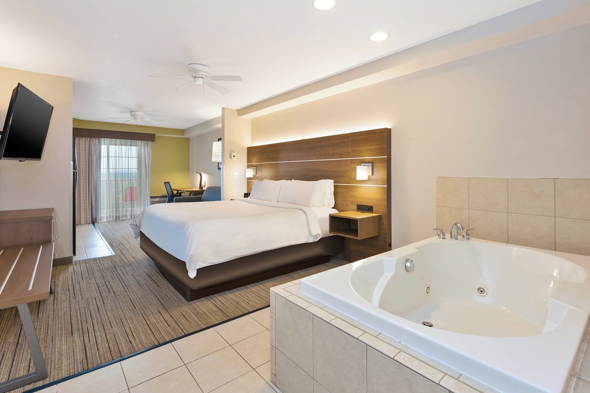 Une chambre d’hôtel équipée d’un lit, d’un bureau, d’une télévision, d’un ventilateur de plafond, d’une grande baignoire et offrant une vue sur l’extérieur.