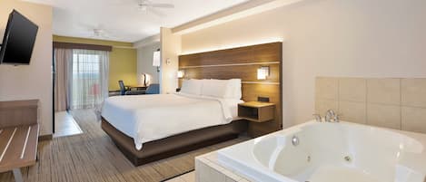 Quarto de hotel com cama, escrivaninha, televisão, ventilador de teto, banheira grande e vista para o exterior.