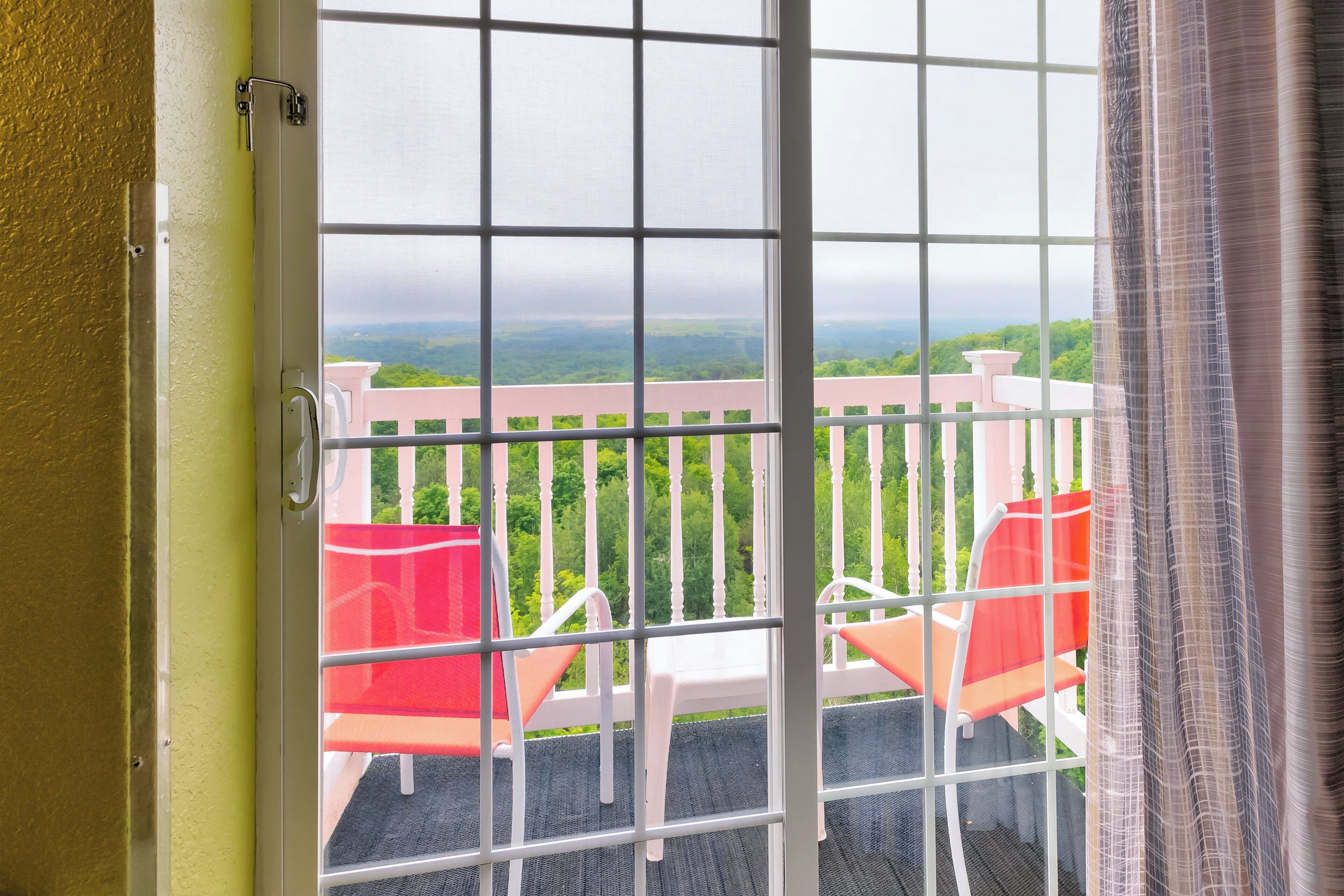 A balcony with a white railing, two chairs, and a view of a green landscape.